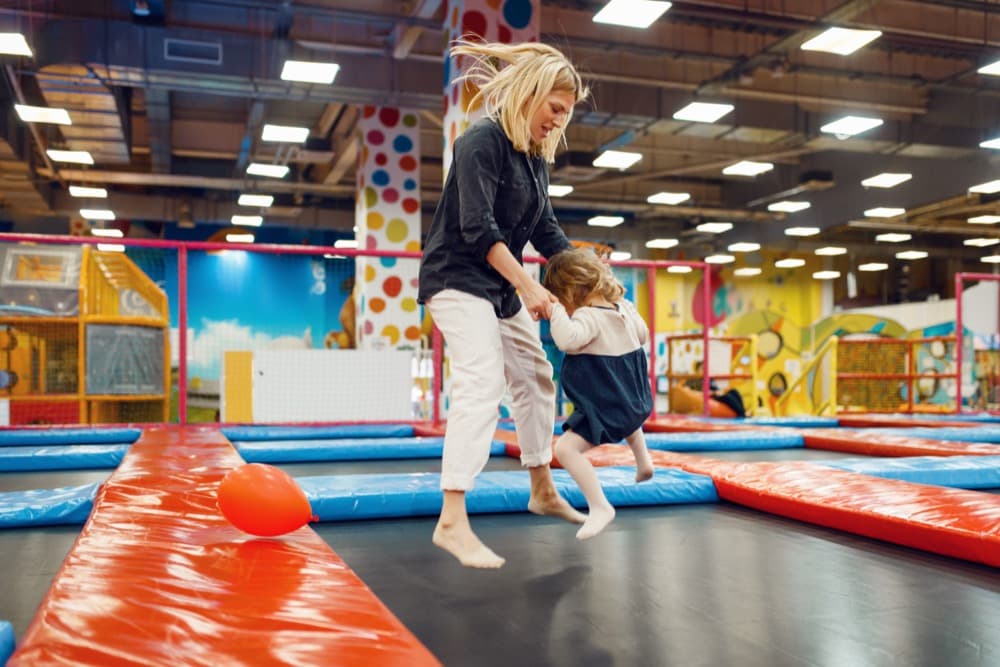 A parent and toddler bouncing together on an indoor trampoline at a family play centre