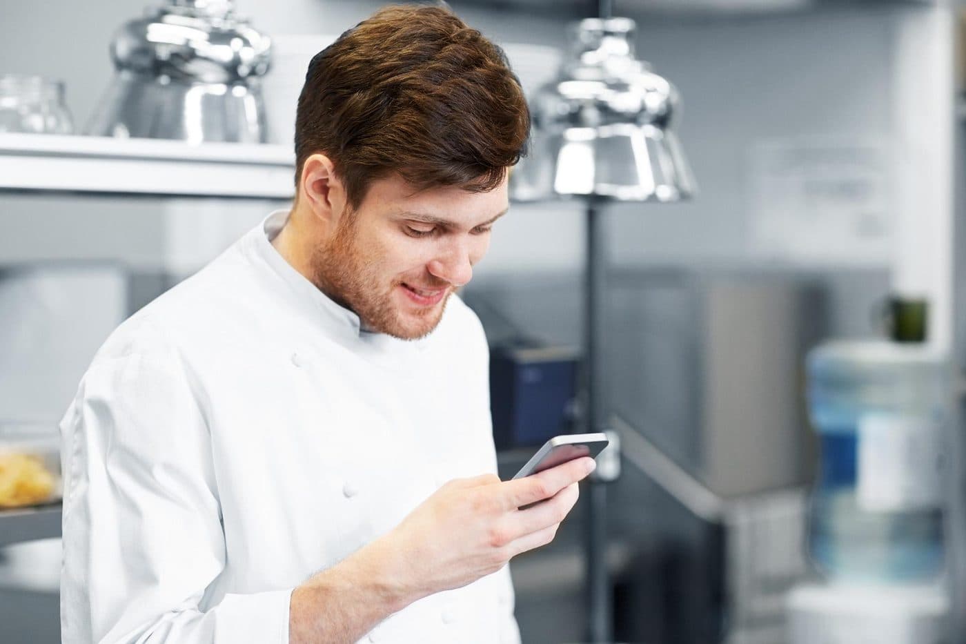 A chef in whites reading something on their phone in a commercial kitchen