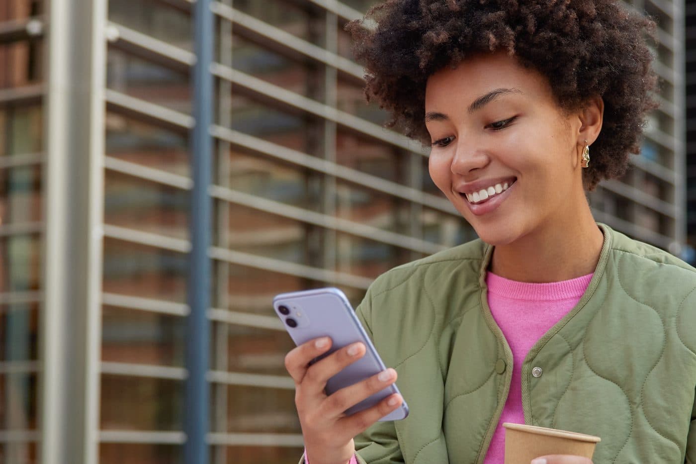 A team member smiling at their phone with a coffee in hand