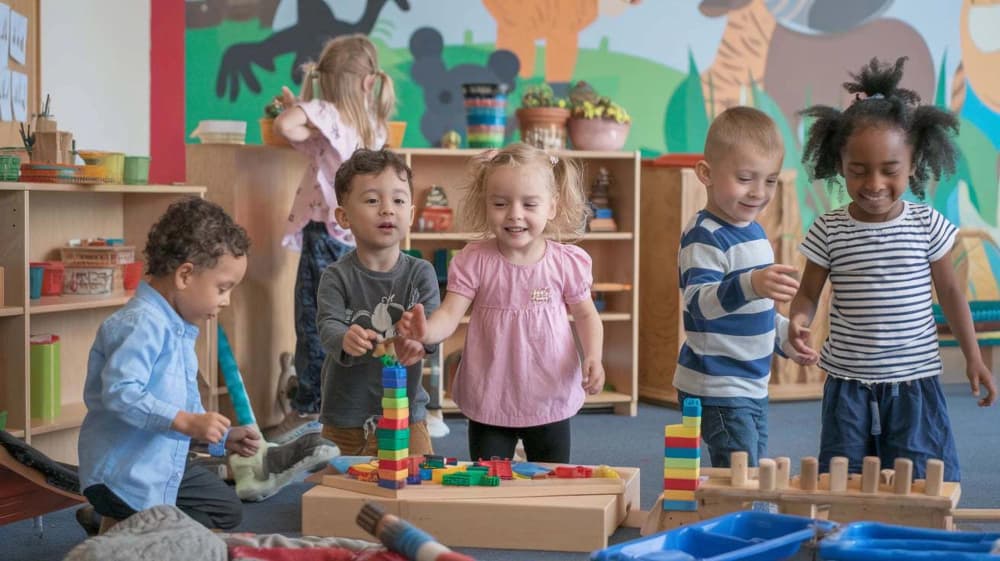 Young children building towers with wooden and plastic blocks in a bright nursery playroom